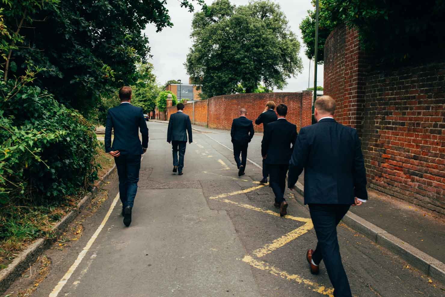 groom and groomsmen walking away down urban street wedding photography in suffolk