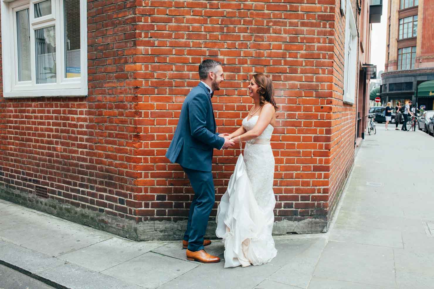 laughing bride and groom against urban brick wall