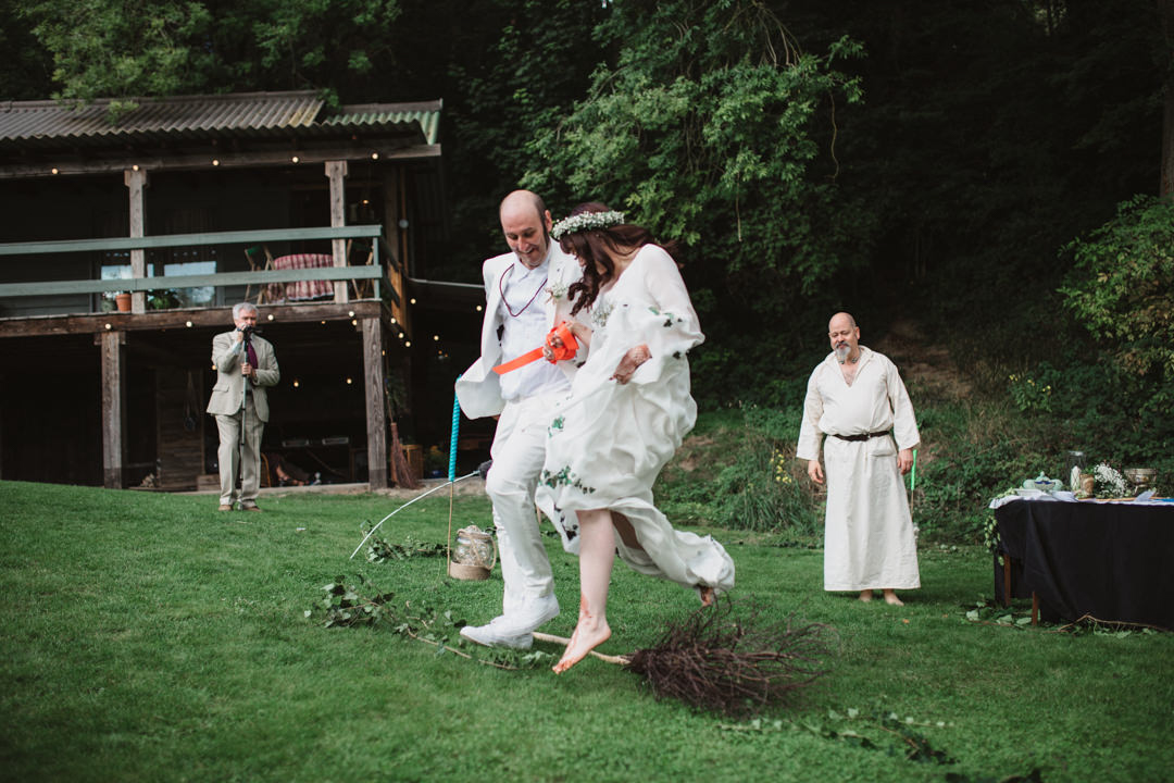 bride and groom dressed in white jumping the broom ceremony outdoors