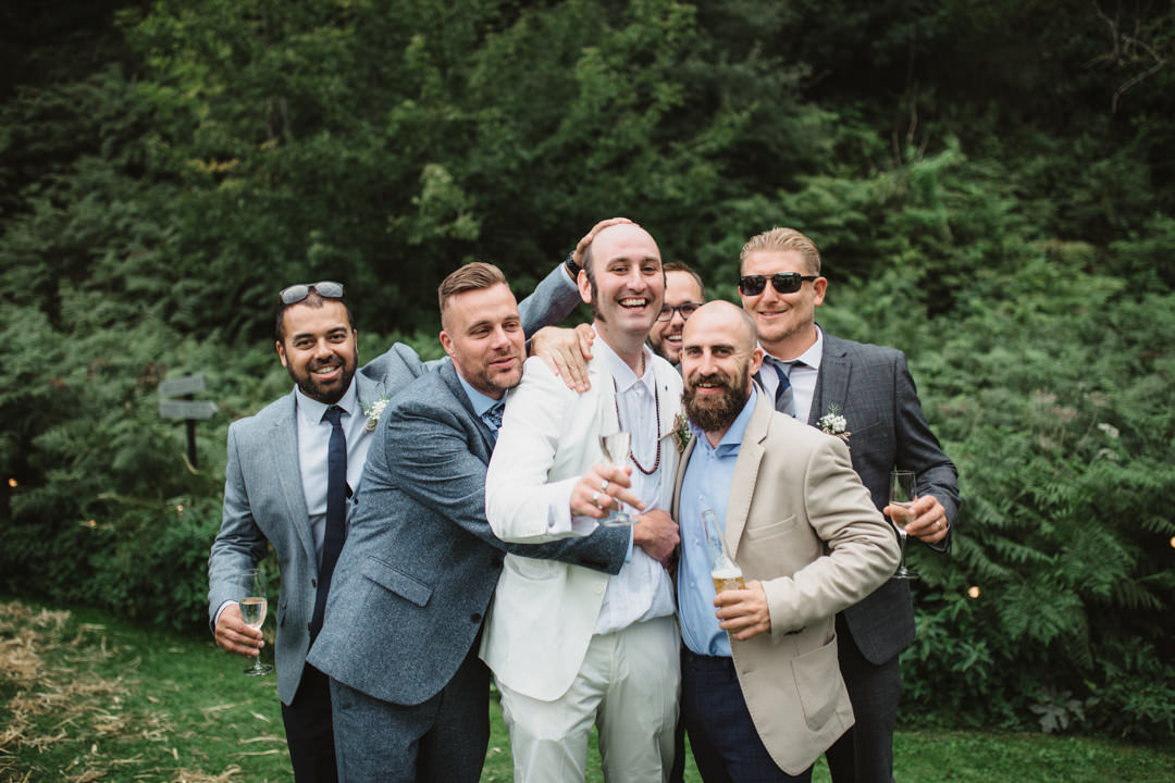 groom wearing white suit being hugged my groomsmen at the keeper and the dell
