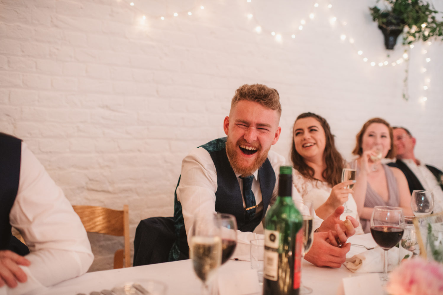 laughing introvert groom during speeches in barn wedding reception