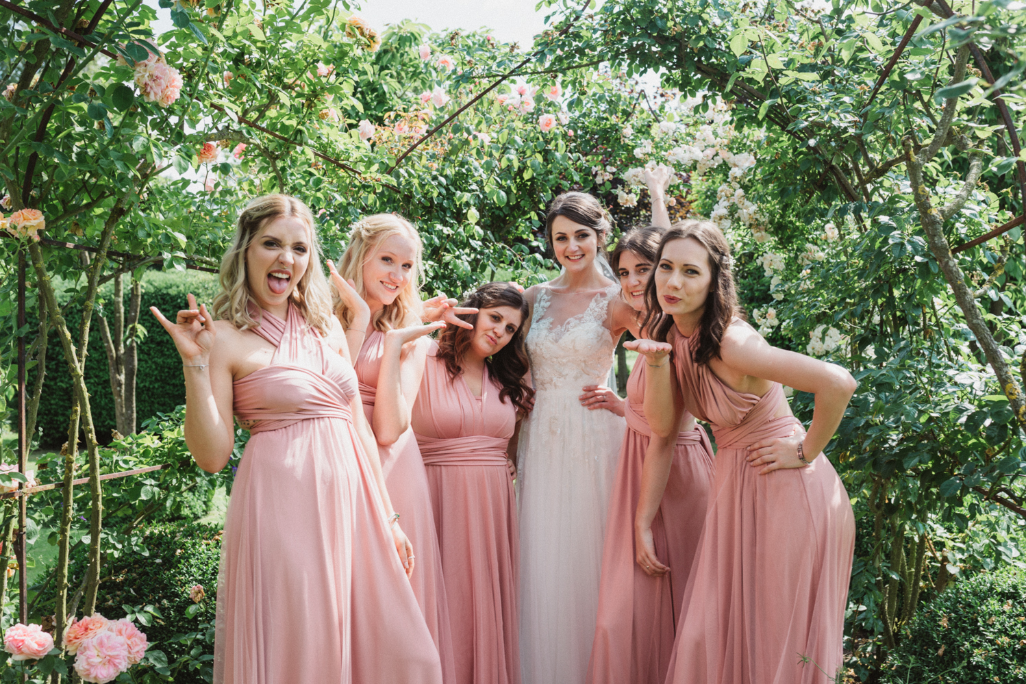 bride and pink bridesmaids laughing at elms barn rose garden in suffolk