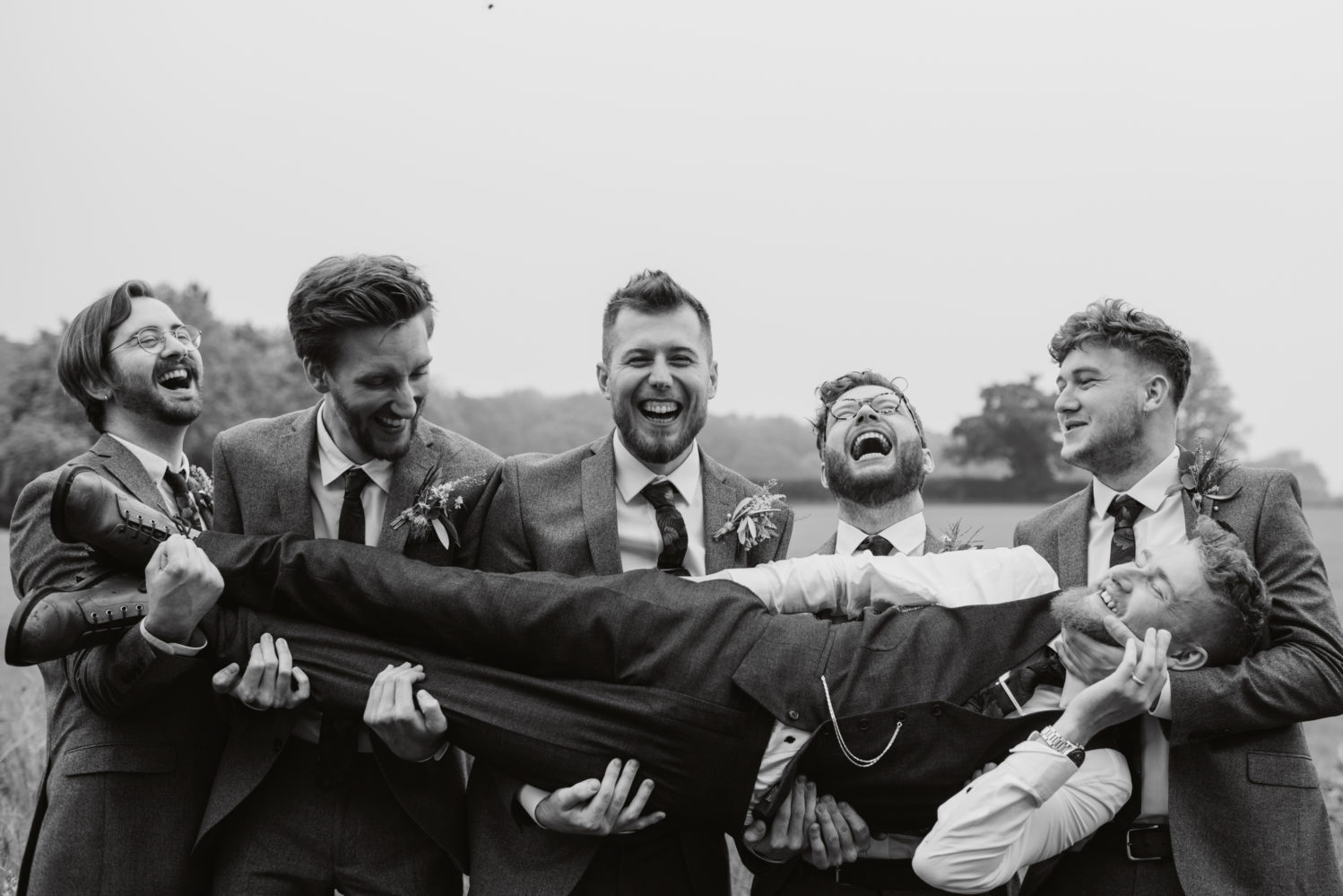 black and white photo of groomsmen holding groom in a suffolk field