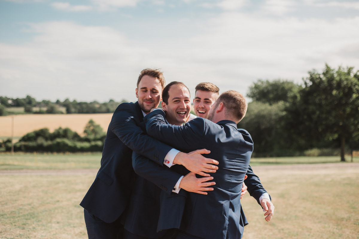 groomsmen hug SUFFOLK BARN WEDDING PHOTOGRAPHY HAWSTEAD